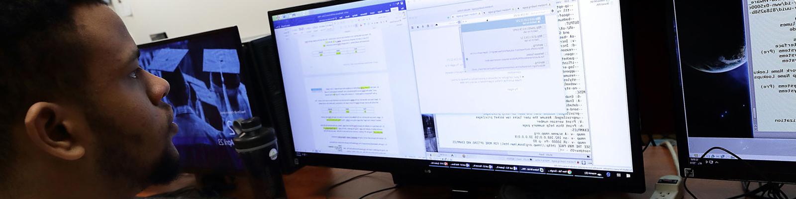 Student using computer with mulitple monitors and white board in background